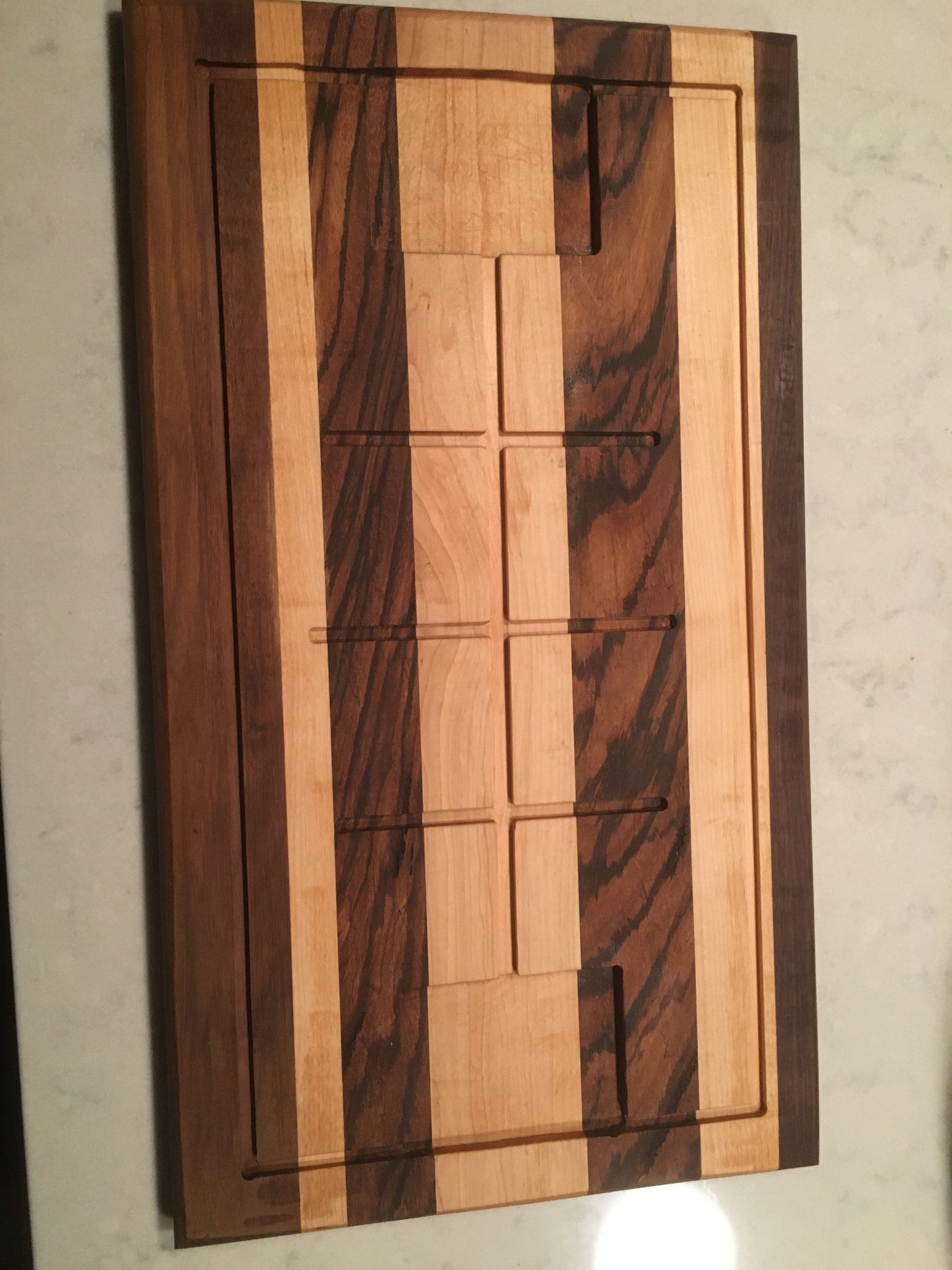 Wooden cutting board with alternating light and dark wood strips in geometric pattern