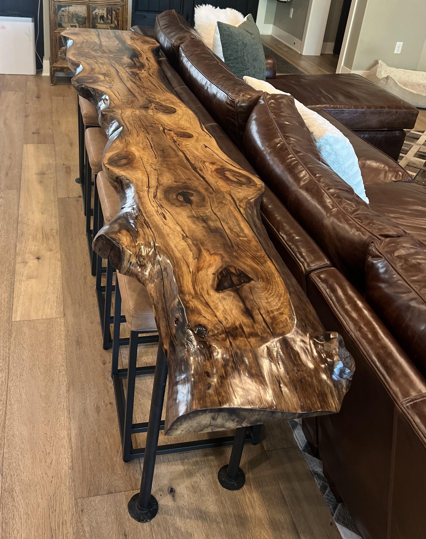 Live edge wood console table with black metal base next to brown leather sofa