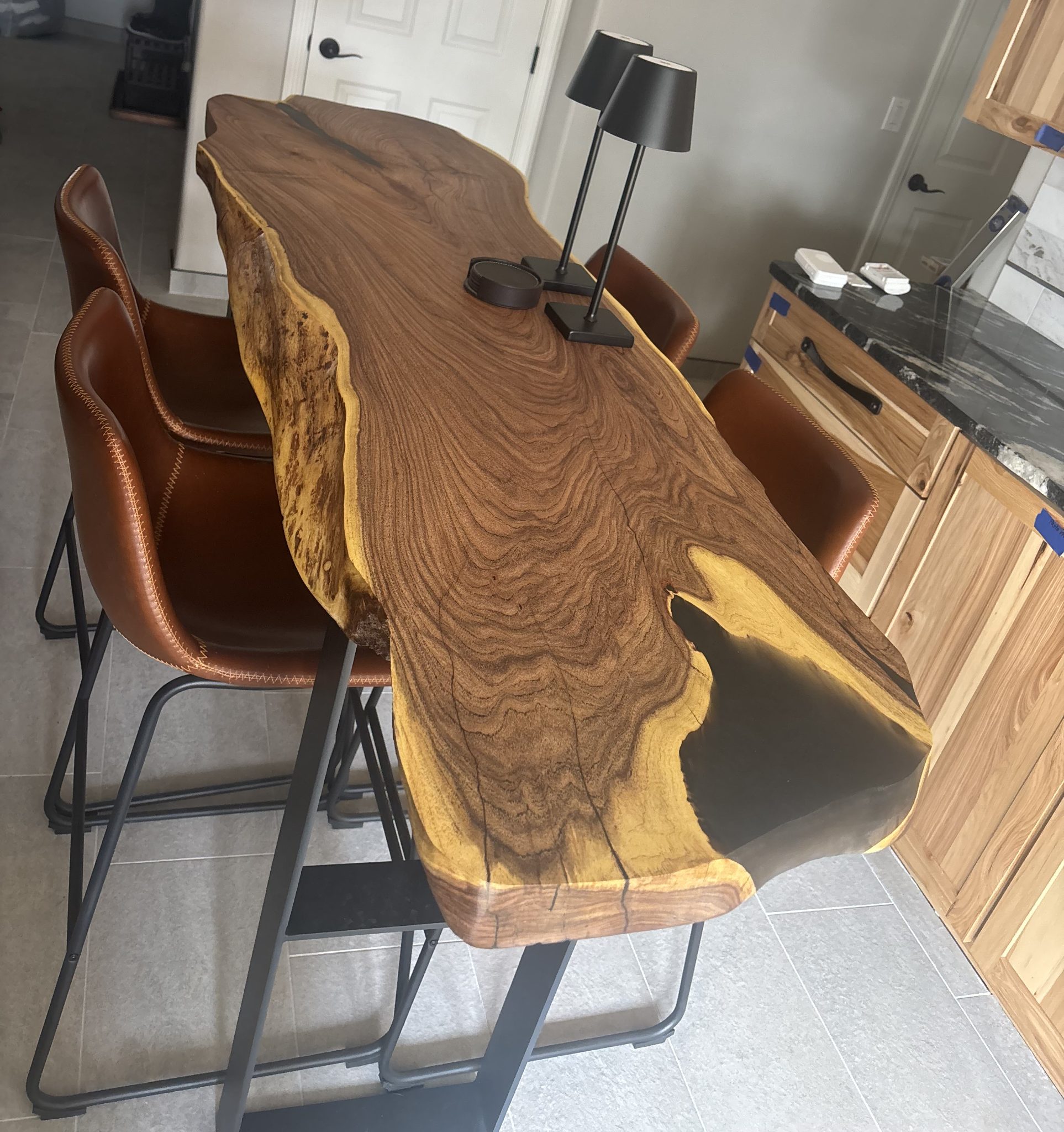 Live edge wood dining table with natural grain patterns and brown leather chairs in modern kitchen
