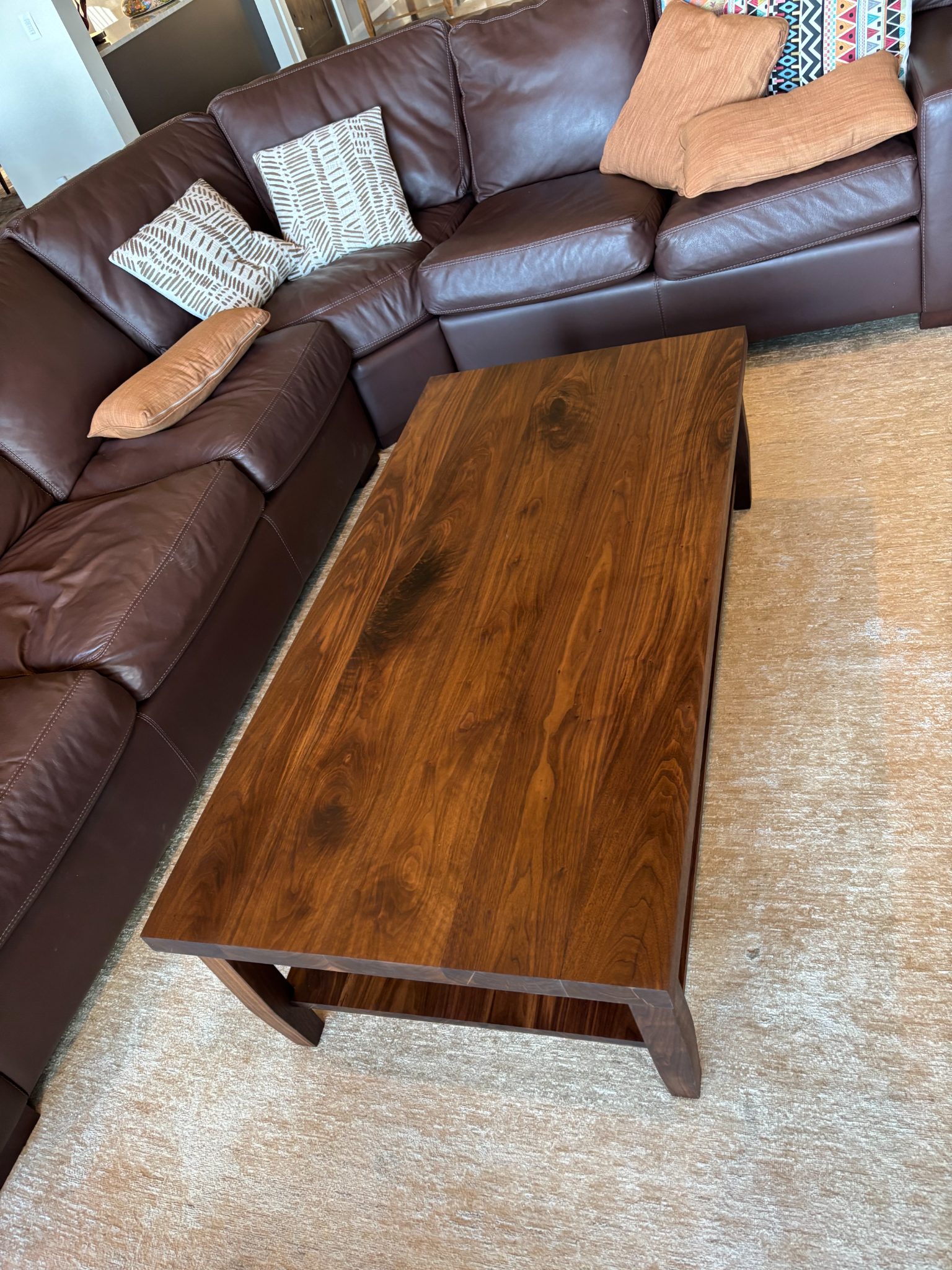 Wooden coffee table in front of brown leather sectional sofa with decorative pillows