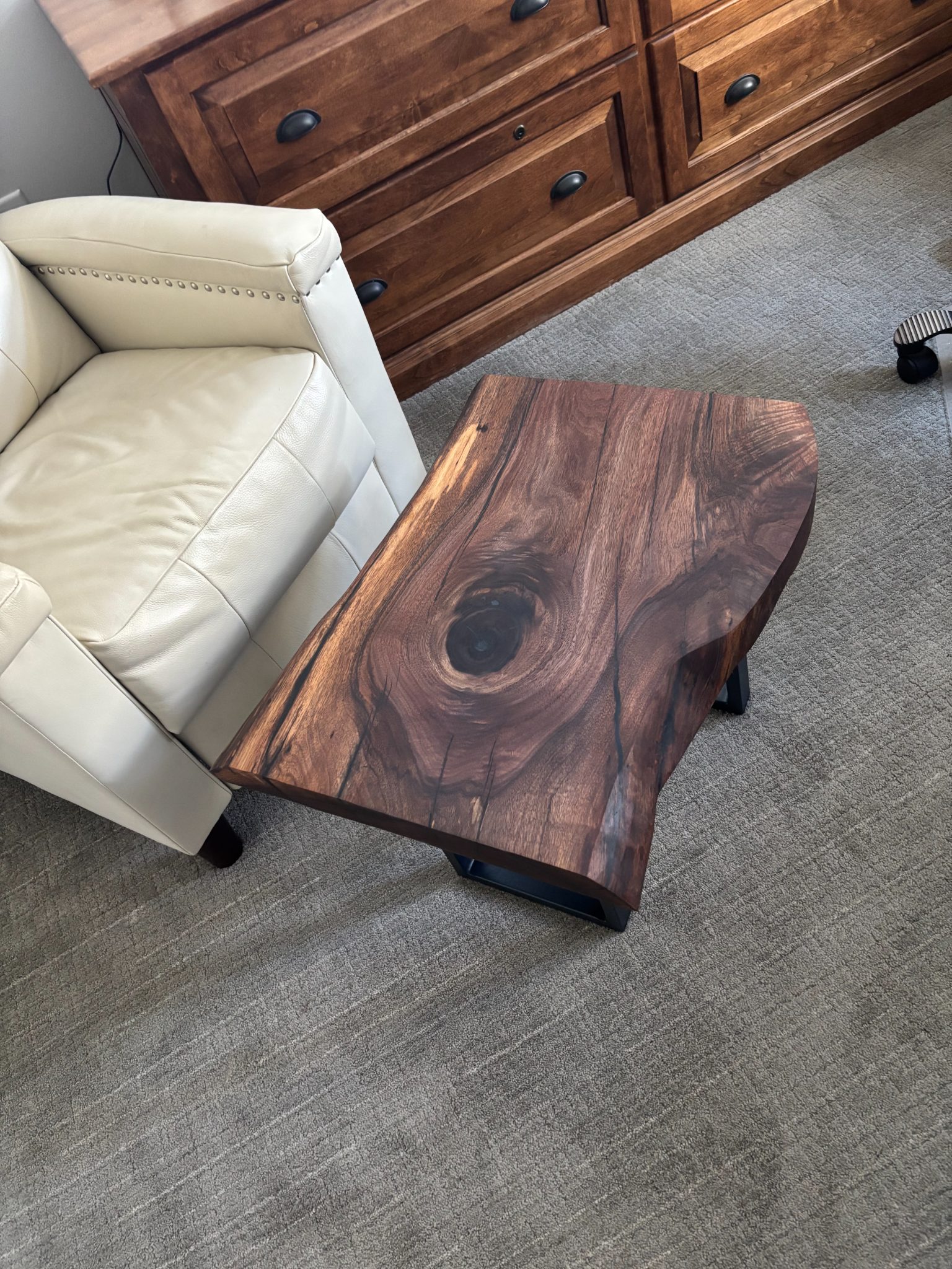 Wooden coffee table with natural grain and knot detail beside cream leather chair and wooden dresser