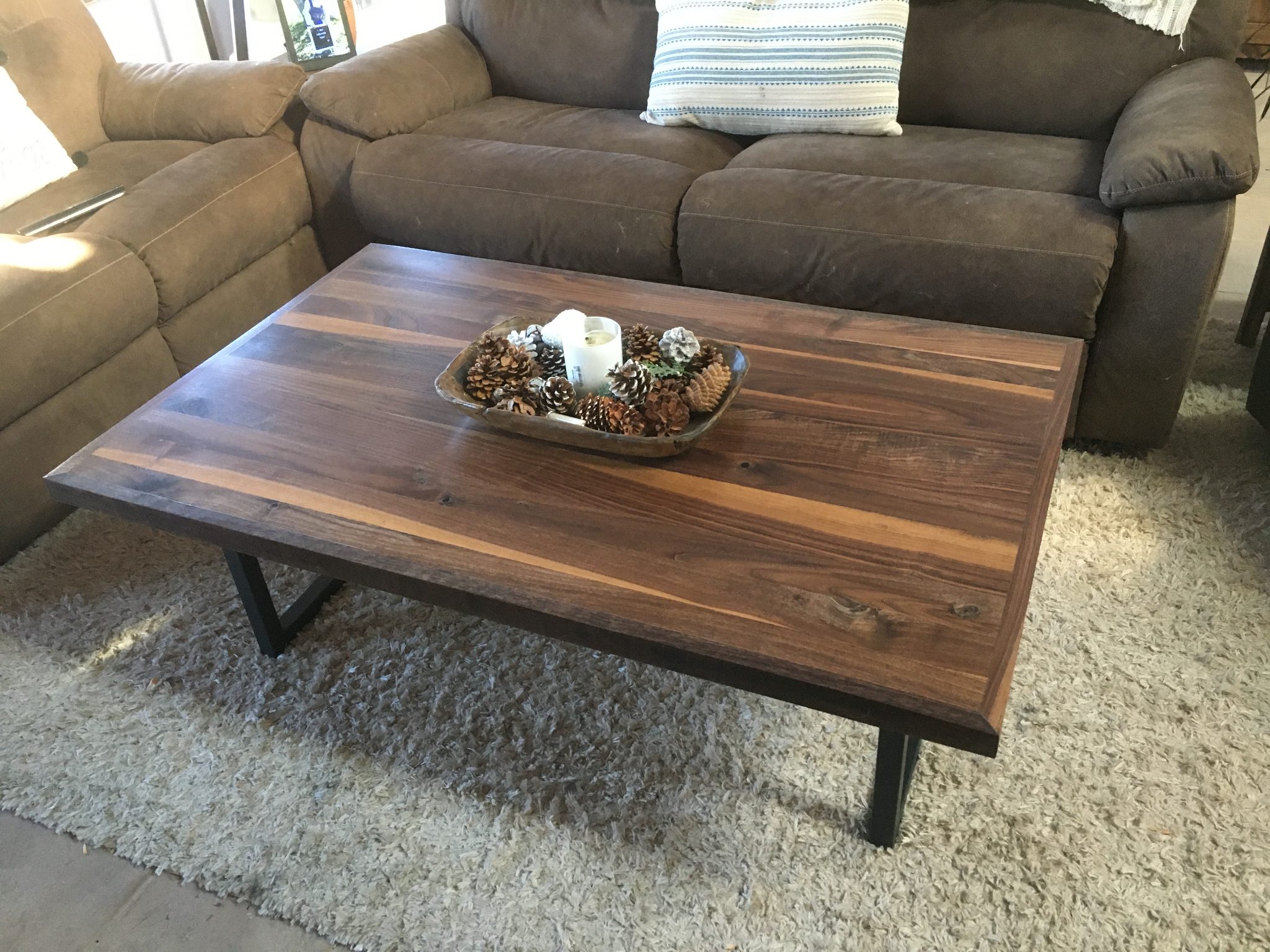 Wooden coffee table with black legs on a light gray rug in front of a gray upholstered sofa