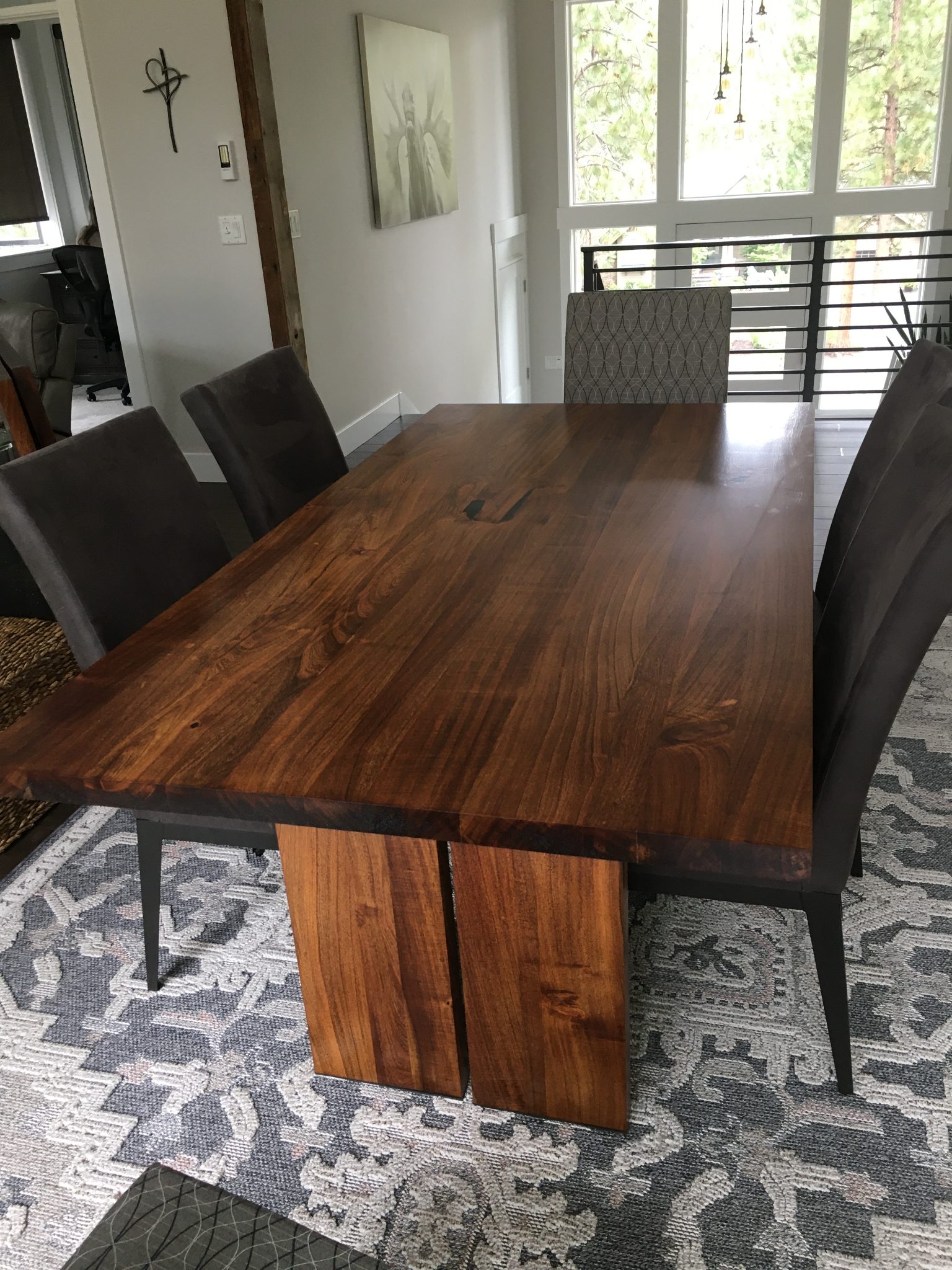 Modern dining room with wooden table and dark upholstered chairs overlooking forest