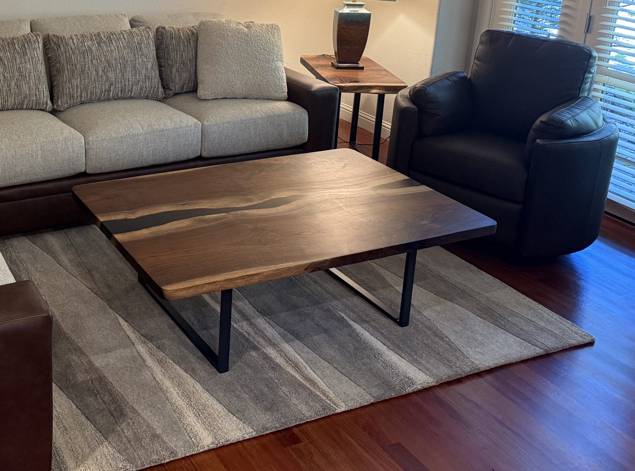 Modern living room with wood coffee table, gray sofa, black leather chair, and area rug