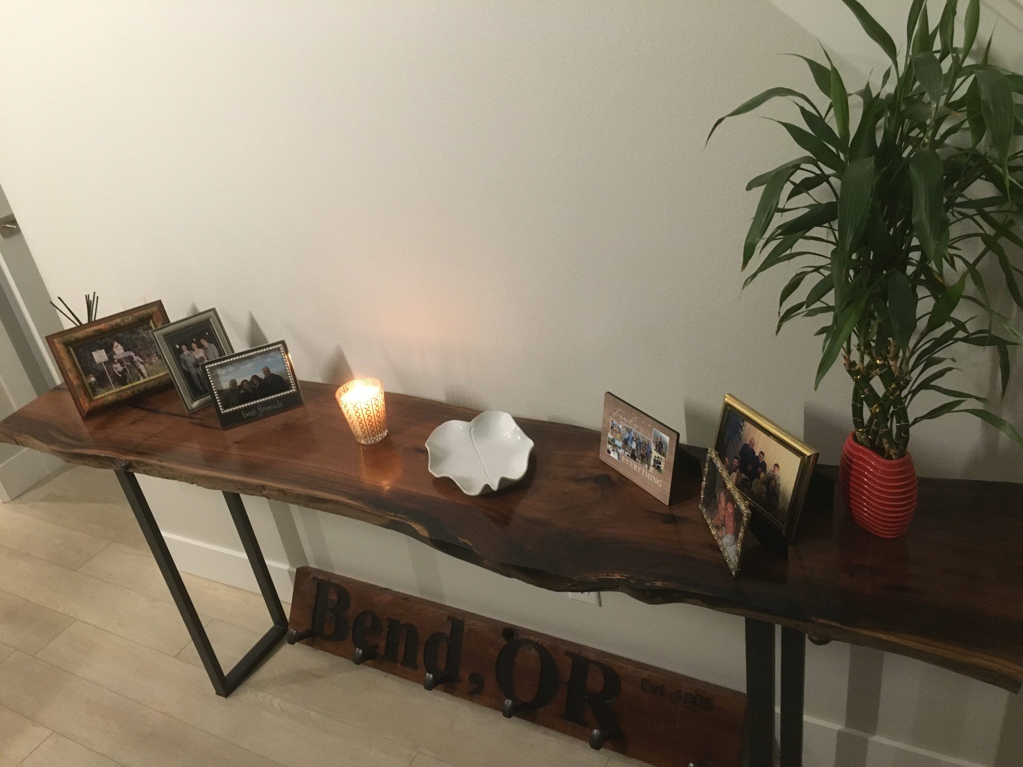 Wooden console table with framed photos, decorative plant, and lighting against white wall