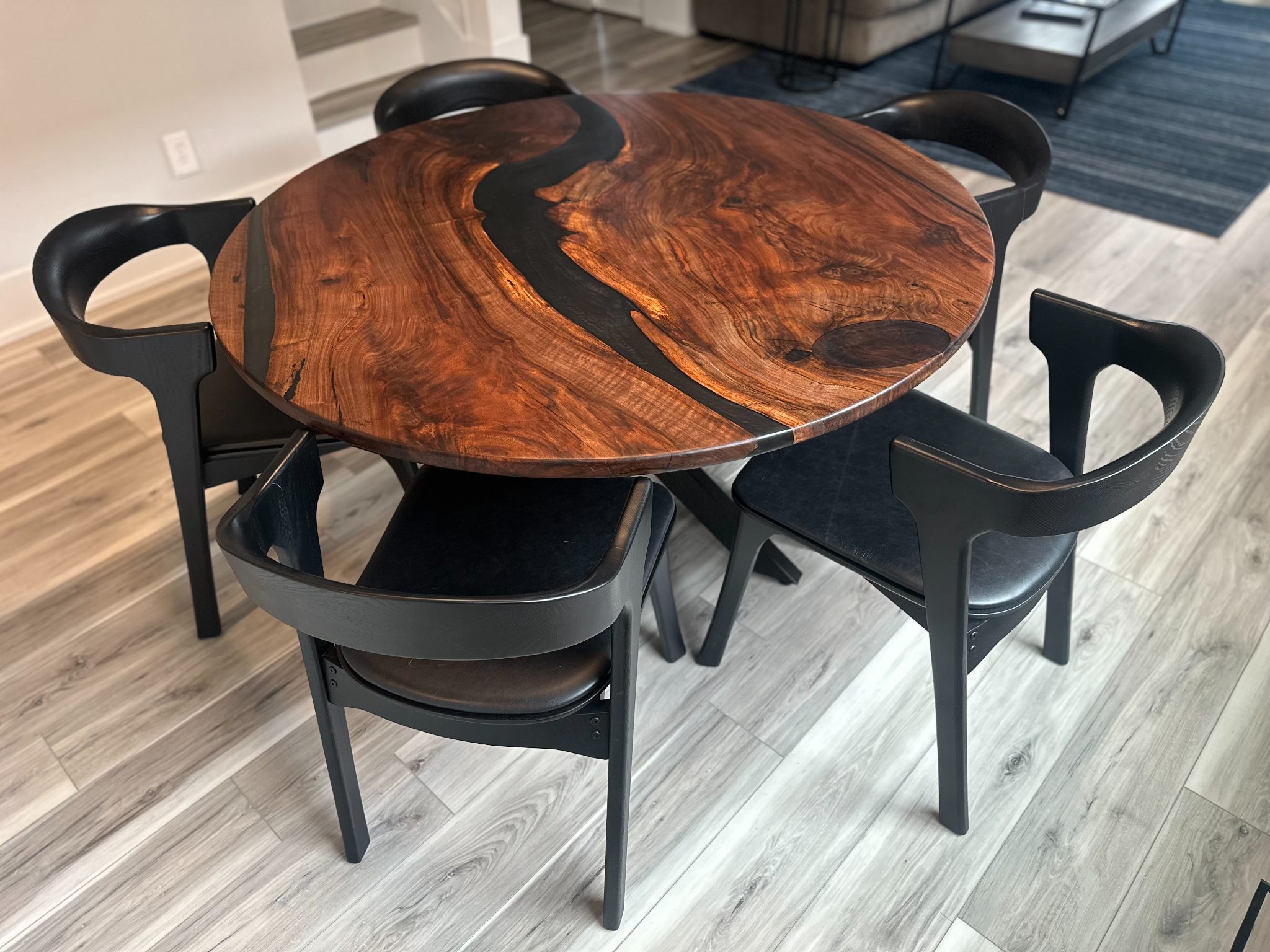 Round wooden table with black epoxy inlay and matching black chairs in modern office space