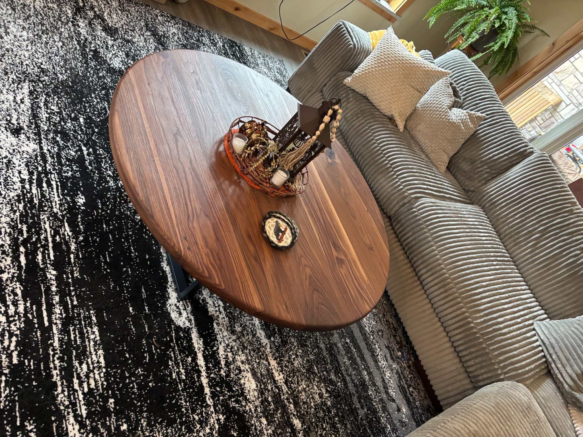 Wooden oval side table with decorative bowl and ornament on striped area rug next to gray sofa