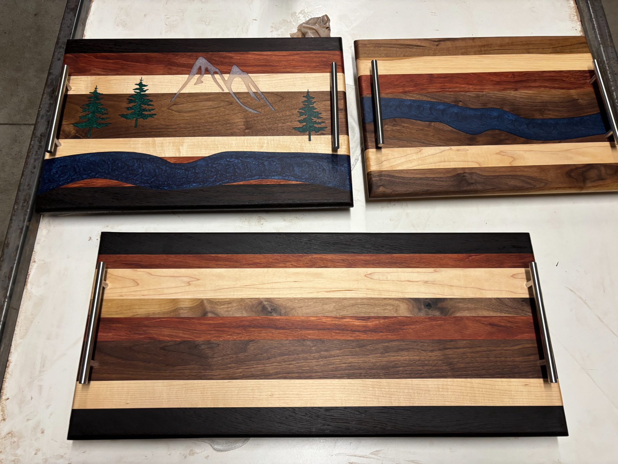 Three wooden serving trays with striped wood designs and metal handles displayed on white surface
