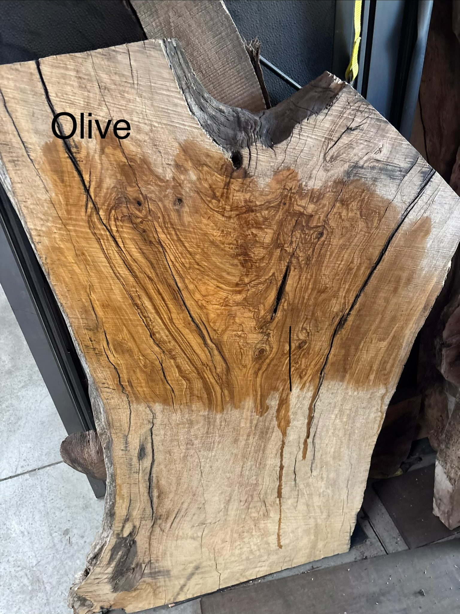Olive wood slab with natural grain patterns and dark streaks displayed indoors